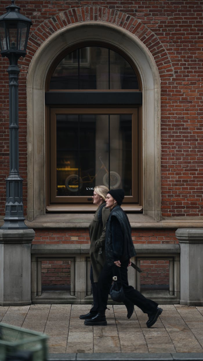 Two adults walking past a vintage brick building facade in a city setting.