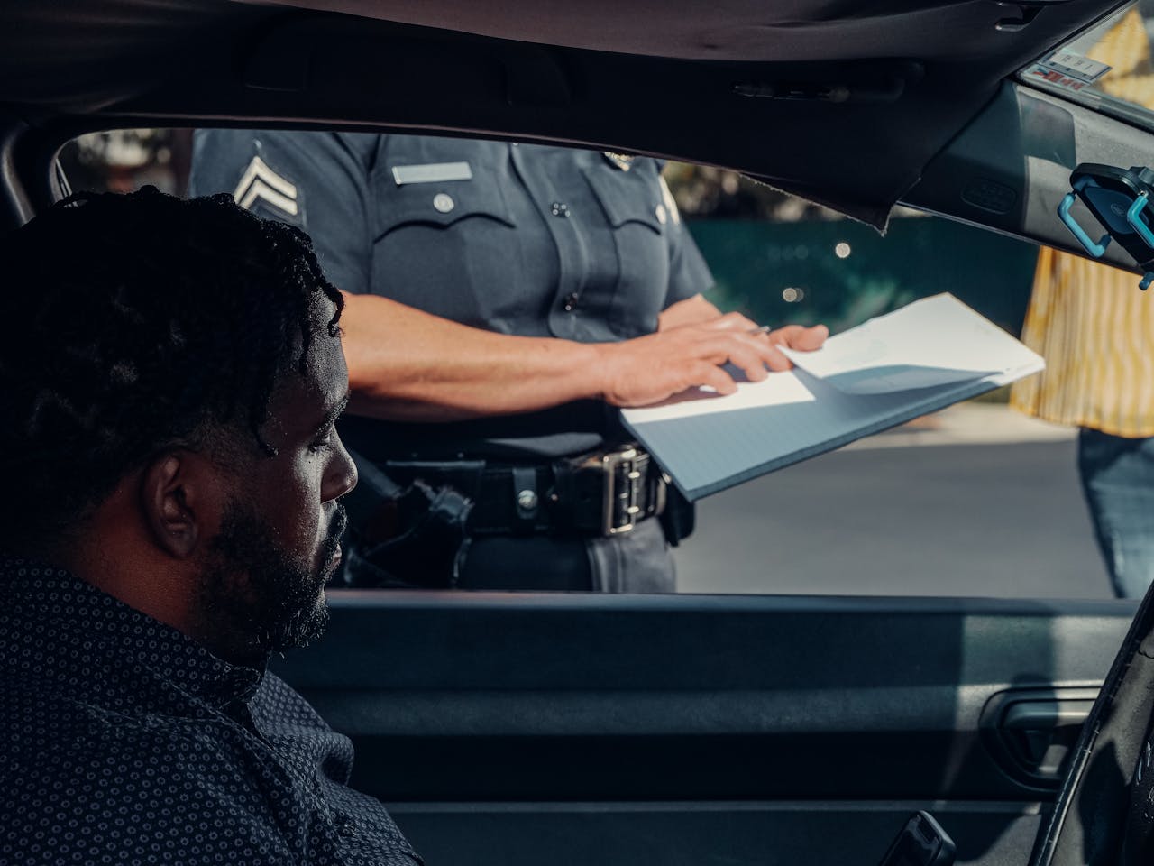 A police officer issues a traffic ticket to a man in a car. Close-up view of the interaction through the window.